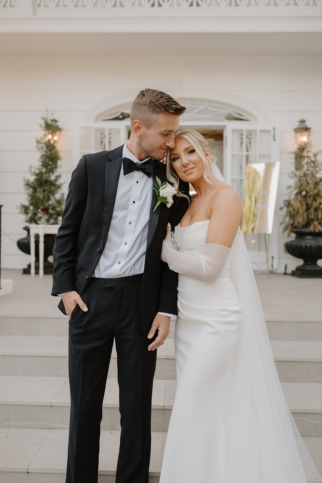 Bride rests her head on the groom's shoulder as they pose tenderly together on the stone steps.